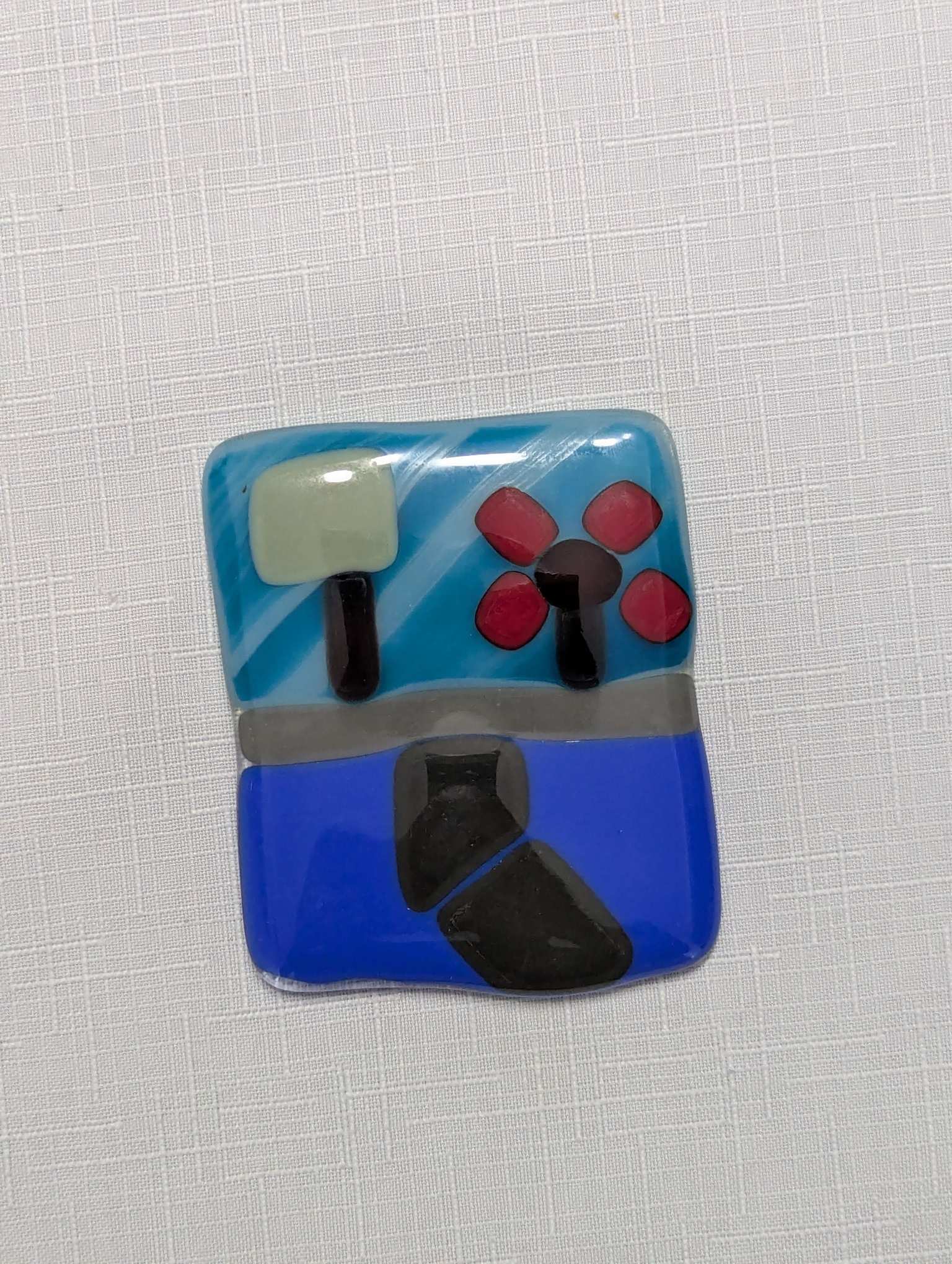 Fused glass landscape of a road with a road crossing a river, with train tracks on the far side, and a forest backdrop. But created by a total beginner, so it's a bit choppy and rectangular.