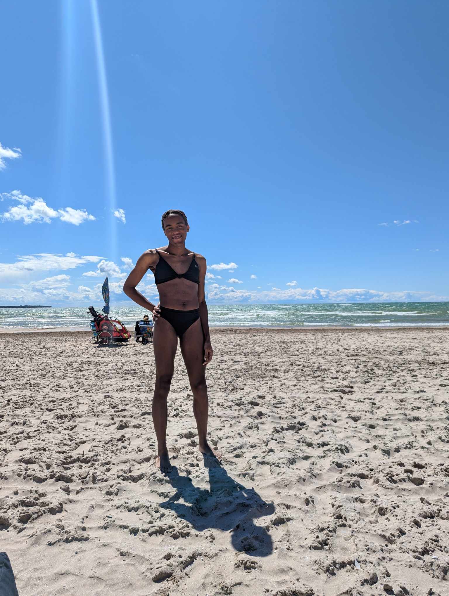Jessica strikes a strong pose and grins at the camera. She's standing on the beach with the water in the background, and her face slightly shadowed by the sun.